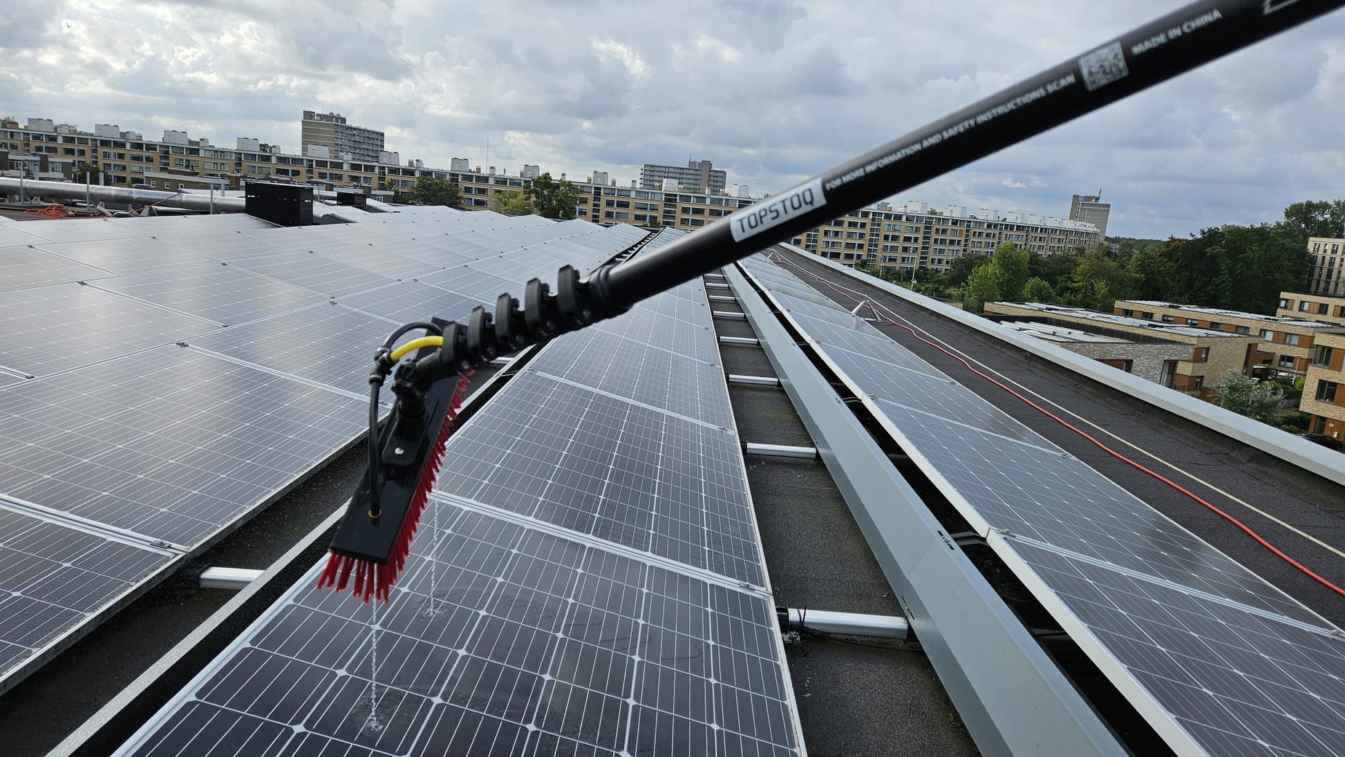 Close-up van de Topstoq carbon telescoopsteel met waterdoorvoerborstel tijdens het schoonmaken van zonnepanelen op een plat dak. Lichtgewicht, stabiel en ideaal voor professioneel onderhoud.