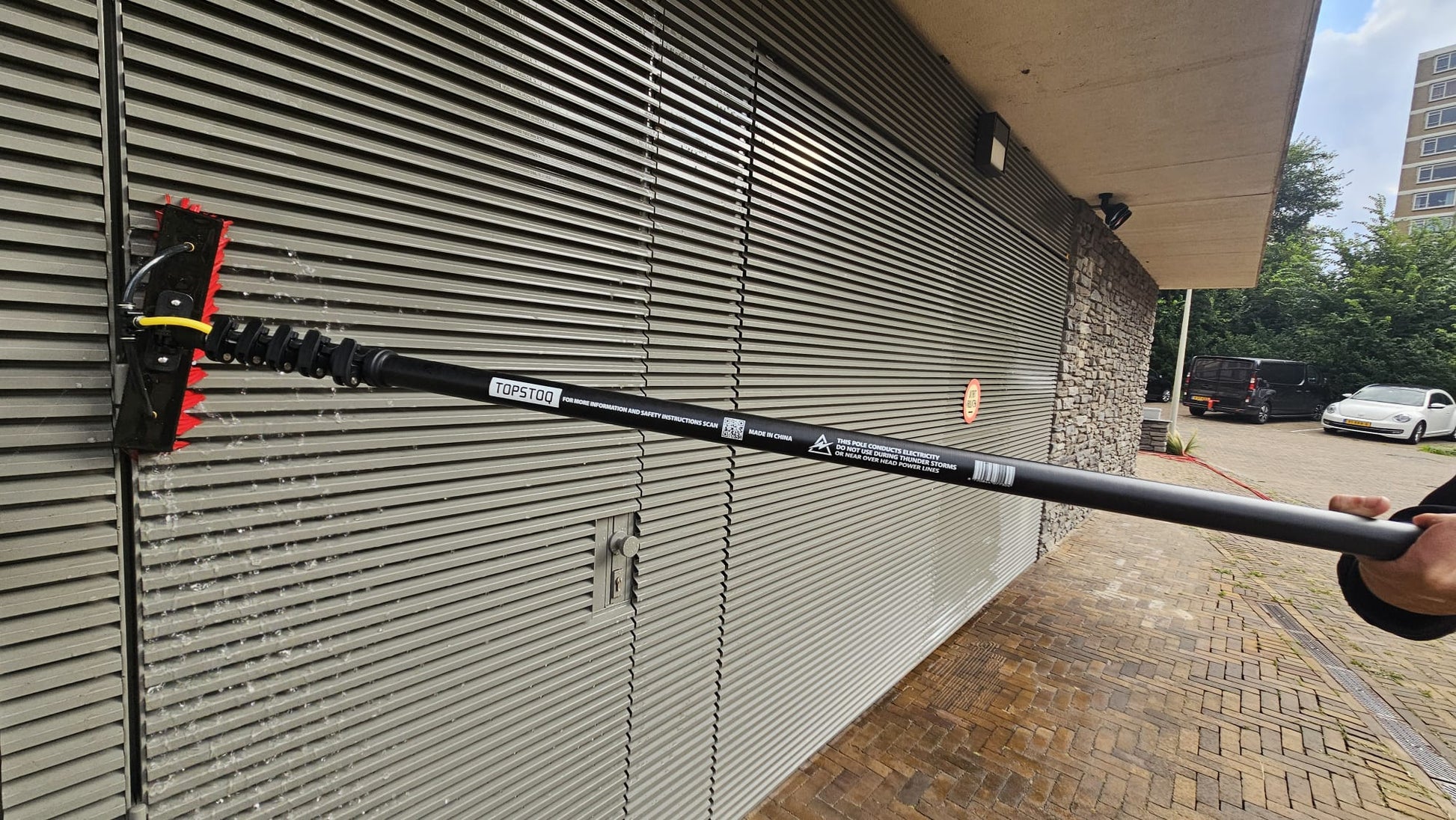 Professionele glazenwasser reinigt metalen gevelbekleding met de Topstoq carbon telescoopsteel en waterdoorvoerborstel. Lichtgewicht, stabiel en ideaal voor gevelreiniging en onderhoud.