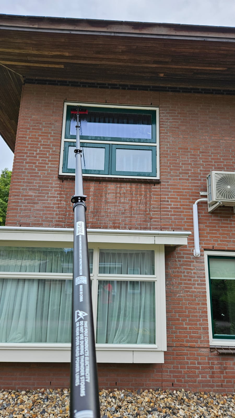 Professionele glazenwasser reinigt een raam op de eerste verdieping met de Topstoq carbon telescoopsteel en waterdoorvoerborstel. Lichtgewicht, stabiel en ideaal voor werken op hoogte.