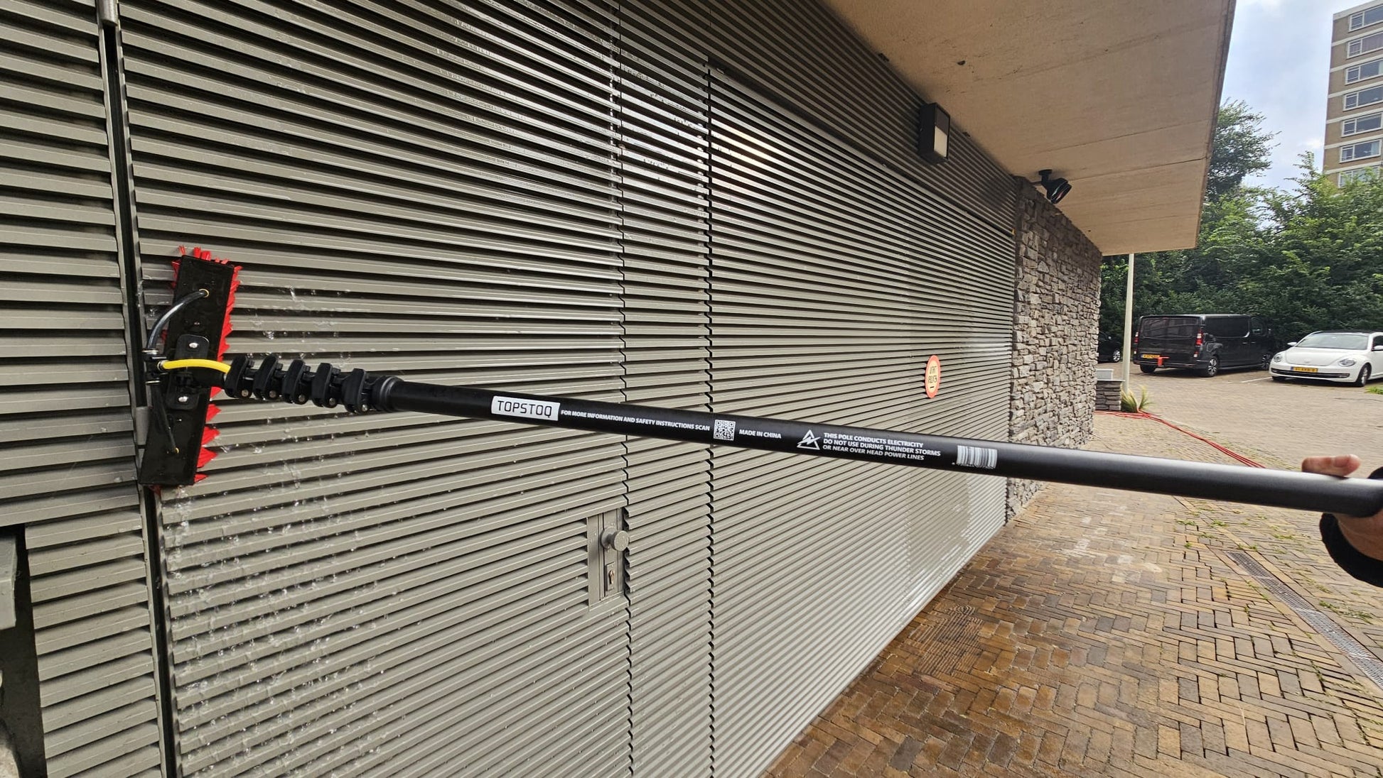 Professionele glazenwasser reinigt metalen gevelbekleding met de Topstoq carbon telescoopsteel en waterdoorvoerborstel. Lichtgewicht, stabiel en ideaal voor gevelreiniging en onderhoud.