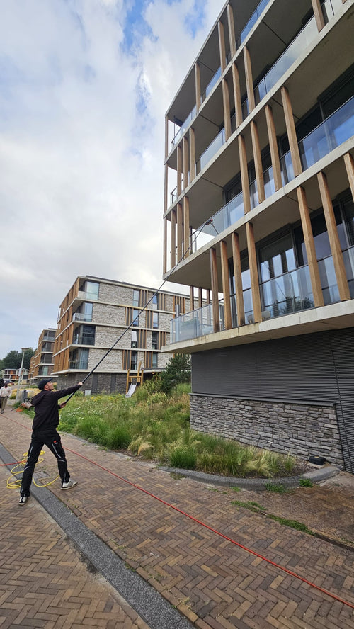 Professionele glazenwasser wast ramen op meerdere verdiepingen van een appartementencomplex met de Topstoq carbon telescoopsteel. Lichtgewicht, stabiel en perfect voor veilig werken op grote hoogte.